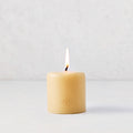 3x3 inch amber pillar candle with a lit cotton wick and gold embossed HG logo on a white surface.