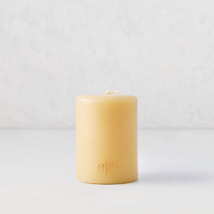 3x4 inch amber unscented pillar candle with a gold embossed HG logo on a white surface.