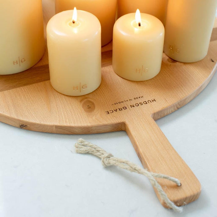 HG Amber unscented 3"x6" paraffin pillar candle with gold HG logo, burning on a wooden board.
