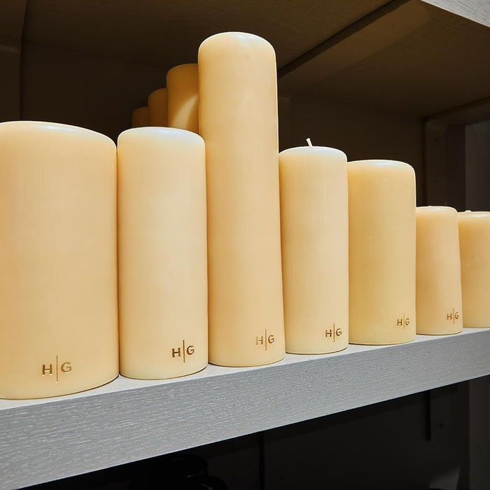 HG Amber Unscented 3"x6" paraffin pillar candle with gold HG logo, on a shelf with other sizes.