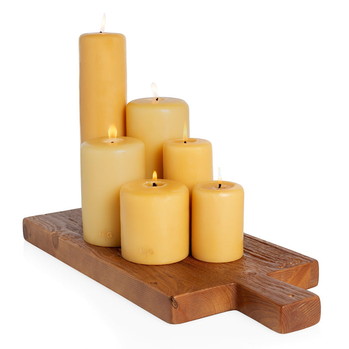 HG Amber unscented paraffin pillar candles, various sizes, with gold HG logo, on a wooden board.