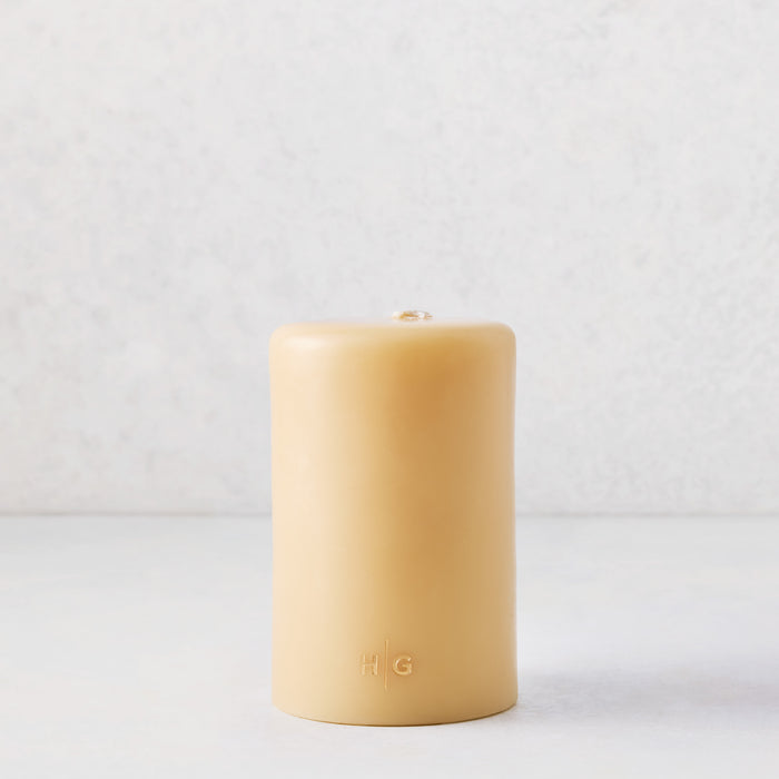 4"x6" hand-dipped amber unscented pillar candle with a gold embossed HG logo on a white background.