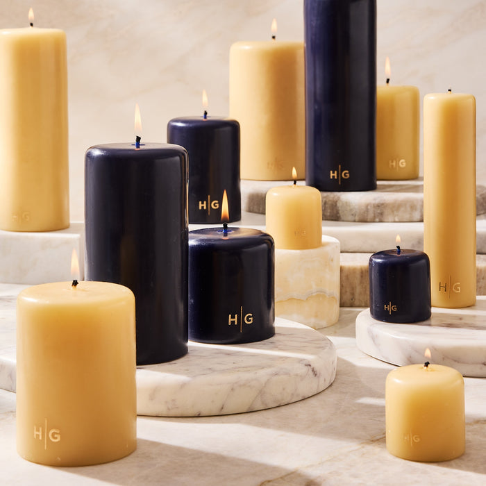 HG Amber Unscented Pillar Candle, 4"x8", with gold HG logo, shown among other amber and black candles.