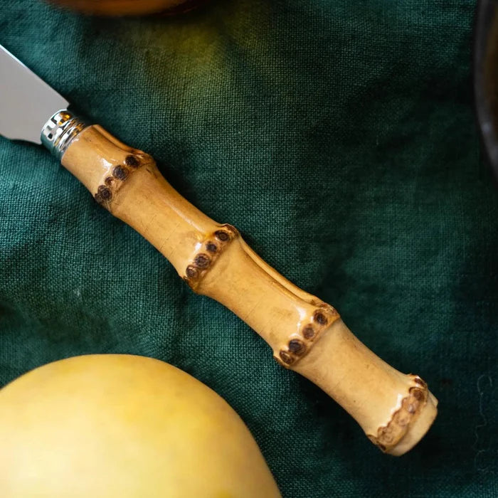 Close-up of a 1940s-inspired bamboo handle on a stainless steel serving knife, on a dark green cloth.