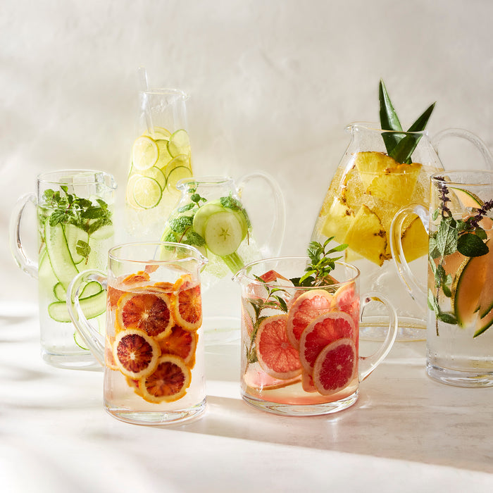 Clear glass cocktail jugs with fruit-infused water, including blood orange, grapefruit, cucumber, and pineapple.