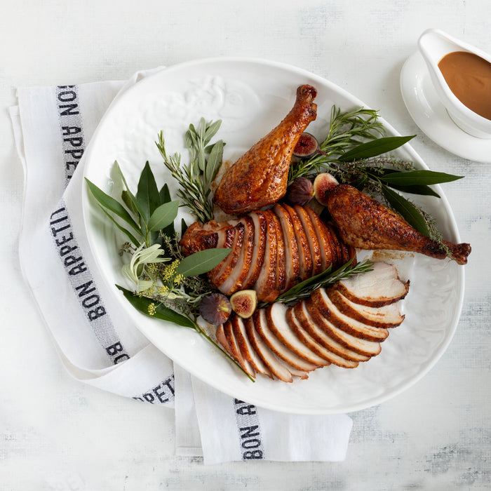 White linen hand towel with "BON APPETIT" text, folded next to a roasted turkey platter.