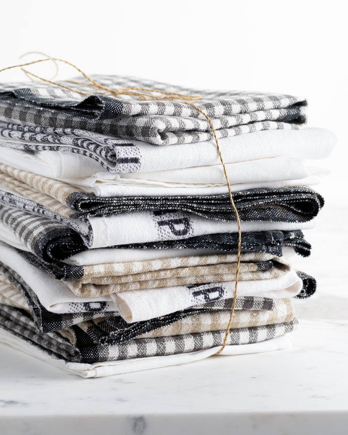 Stack of black, white, and beige linen hand towels with plaid and striped patterns, tied with twine.