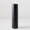 3x12 inch black unscented pillar candle with a gold HG logo and a lit cotton wick.