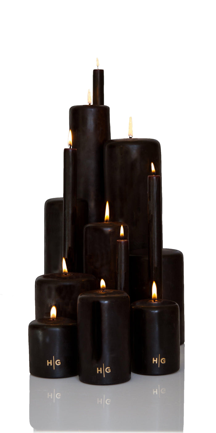 HG Black unscented pillar candles, various sizes, with gold HG logo and lit wicks.