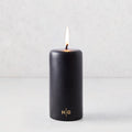 3x6 inch black unscented pillar candle with a burning wick and gold HG logo on a light grey background.