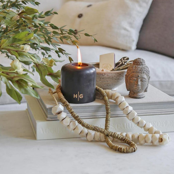 HG Black Unscented Pillar Candle, 3"x6", with gold HG logo, burning on books with decor.