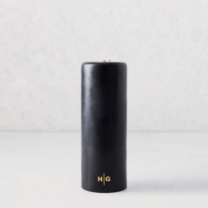 3x8 inch black unscented pillar candle with a gold HG logo embossed on the base, set against a light background.