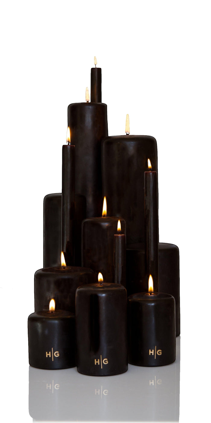 Collection of various sized HG black pillar candles with gold embossed logos, all burning.
