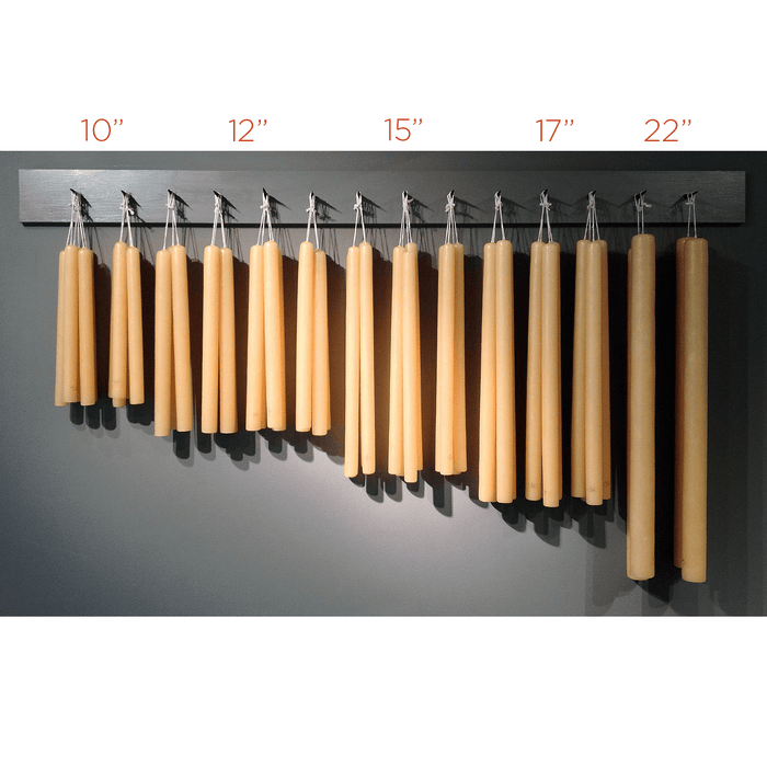 Five sets of unscented amber taper candles in varying heights from 10" to 22", hanging on a dark rack.