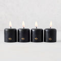 Set of four 2-inch black unscented votive candles with lit wicks and gold embossed HG logo on a light background.