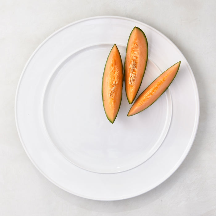 White Bolinas Round Trimmed Ceramic Serving Platter with three cantaloupe slices.