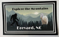 A bumper sticker with an illustration of a white squirrel and Sasquatch, featuring the text 'Explore the Mountains, Brevard, NC'.