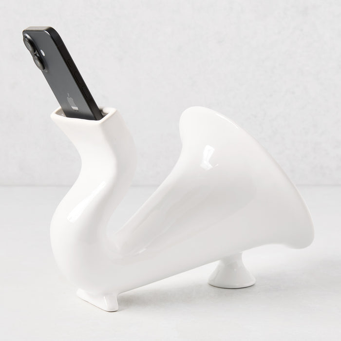 White ceramic speaker, 10"L, with a black smartphone inserted, featuring a curved, horn-like design.