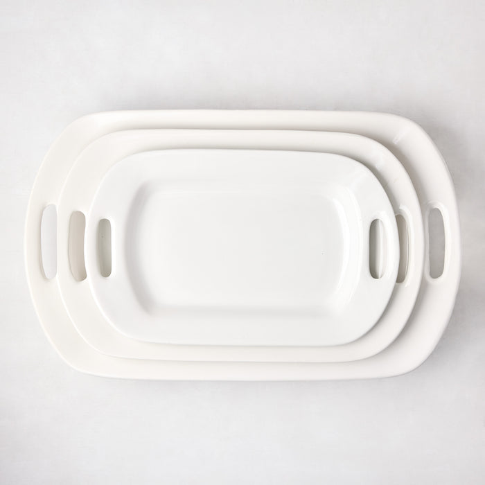 Three white ceramic serving platters with handles, stacked from largest to smallest.