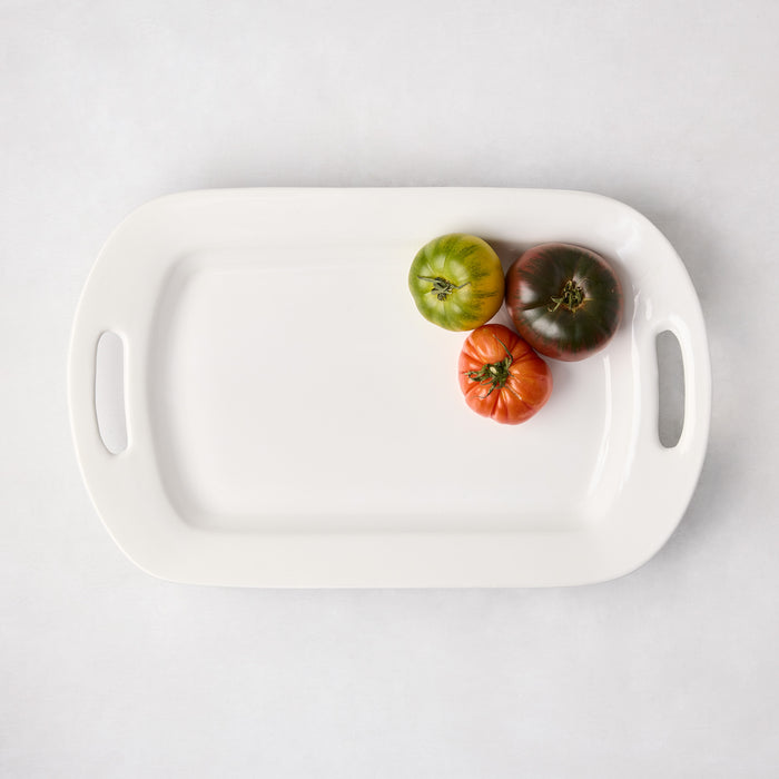 White ceramic serving platter with handles, holding three heirloom tomatoes.