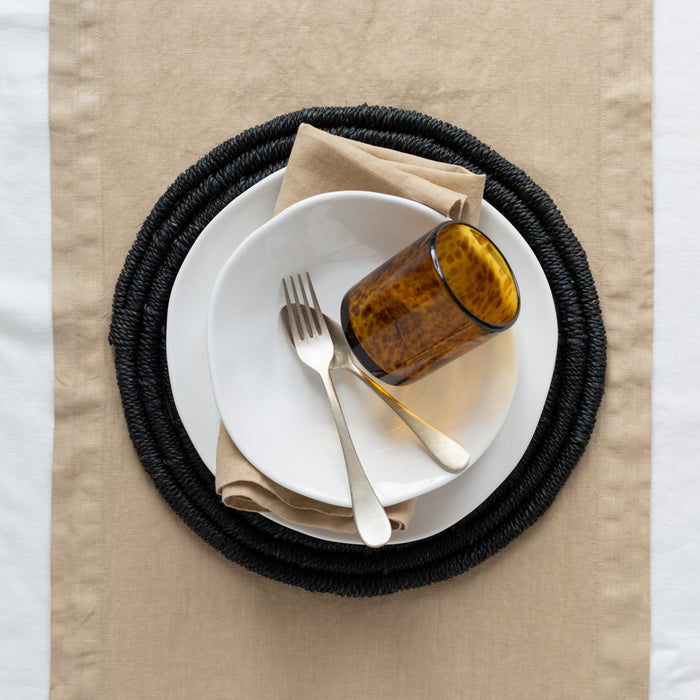 Chai HG Signature hand-dyed linen napkin, 22" square, folded under white plates with a glass and forks.