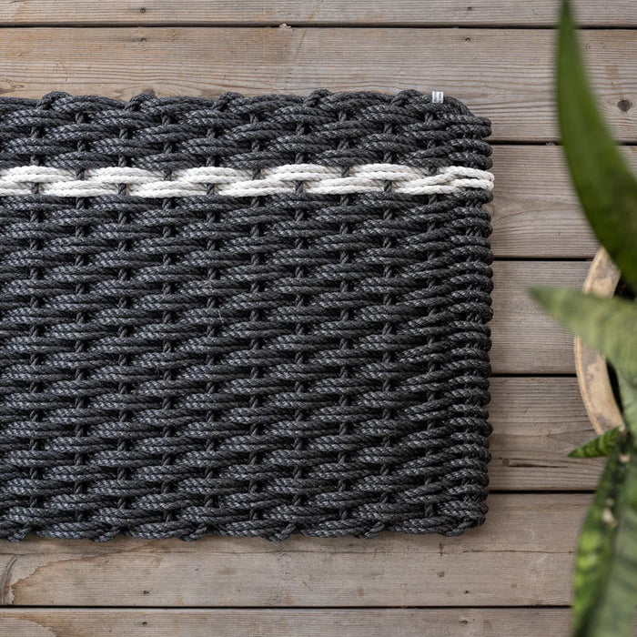 Handwoven charcoal rope doormat with a single white pearl stripe, on a wooden deck.