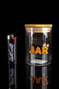 Glass cannabis jar with orange buds and a branded lighter, displayed on a reflective surface.
