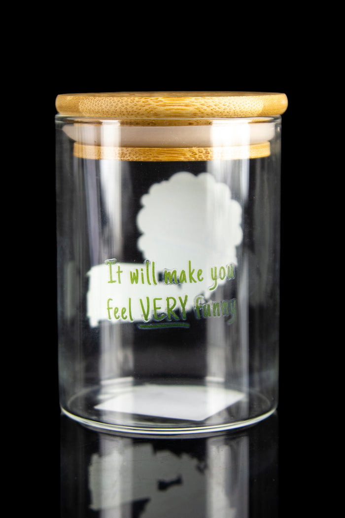 Clear glass jar with a bamboo lid displaying a humorous message about cannabis effects, reflecting on a mirrored surface.