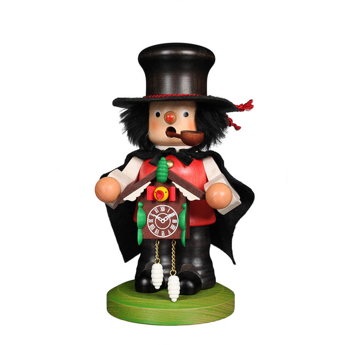 Handcrafted German smoker figurine dressed as a Black Forest fellow, holding a cuckoo clock, wearing a black top hat with a red band, a light red buttoned vest over a white shirt, a flowing black felt cape, and black pants and shoes.