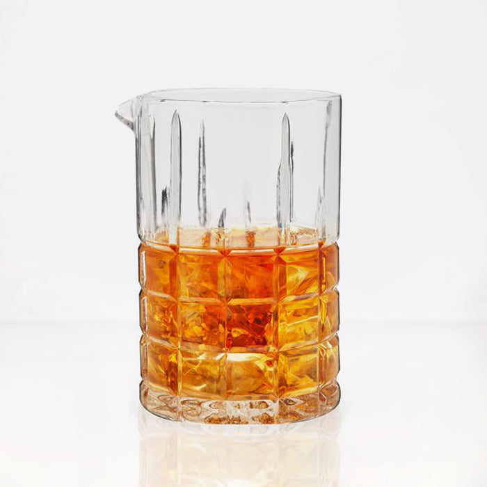 Clear square-cut crystal cocktail mixing glass with a pour spout, filled with amber liquid and ice.