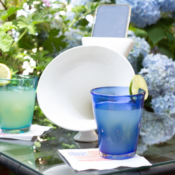 Dark blue 8 oz. Henri glass with a lime slice, next to a green glass and white bowl on a glass table.