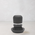 Dark grey soap dispensing dish brush with polyester bristles and clear reservoir on a matching stand.