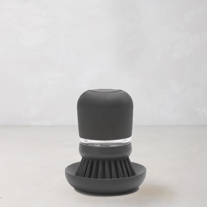 Dark grey soap dispensing dish brush with polyester bristles and clear reservoir on a matching stand.