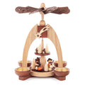 This beautiful, hand carved Christmas pyramid holds a candle on each of the sides of its base to provide gentle lighting on every side when in use. The heat from the candles causes the top propeller in the center of the pyramid to turn. There are trees and woodsmen who are carrying wood and knapsacks on the bottom main platform and smaller trees and mushrooms on the smaller upper platform.