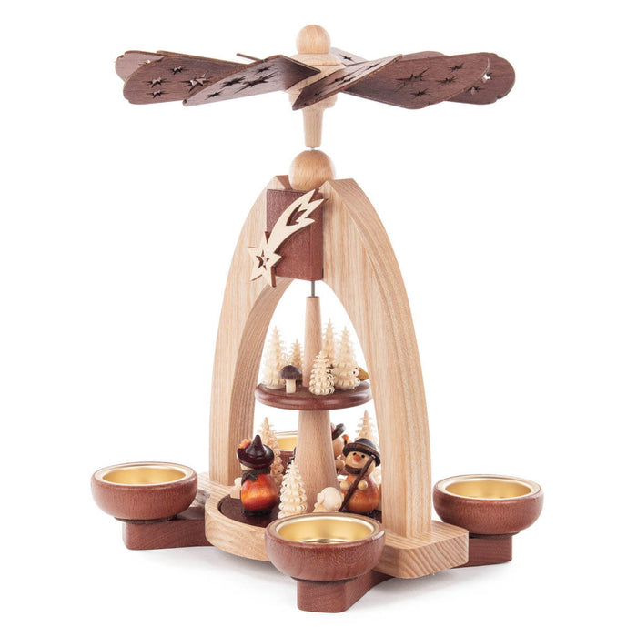 This beautiful, hand carved Christmas pyramid holds a candle on each of the sides of its base to provide gentle lighting on every side when in use. The heat from the candles causes the top propeller in the center of the pyramid to turn. There are trees and woodsmen who are carrying wood and knapsacks on the bottom main platform and smaller trees and mushrooms on the smaller upper platform.