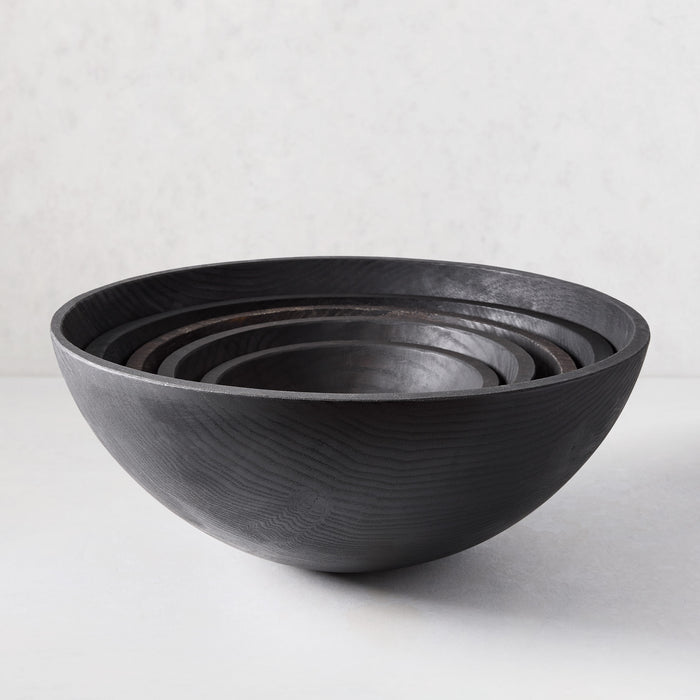 Set of four ebonized wood bowls, dark with visible wood grain, nested on a light surface.
