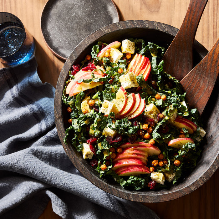 Ebonized wood bowl, 11", holding a kale salad with apples, cranberries, and feta, on a wooden table.