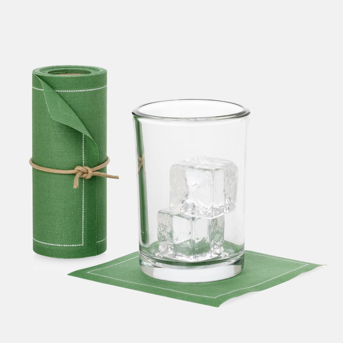 Roll of 50 eucalyptus green cotton cocktail napkins with white stitching, next to a glass with ice on a single napkin.