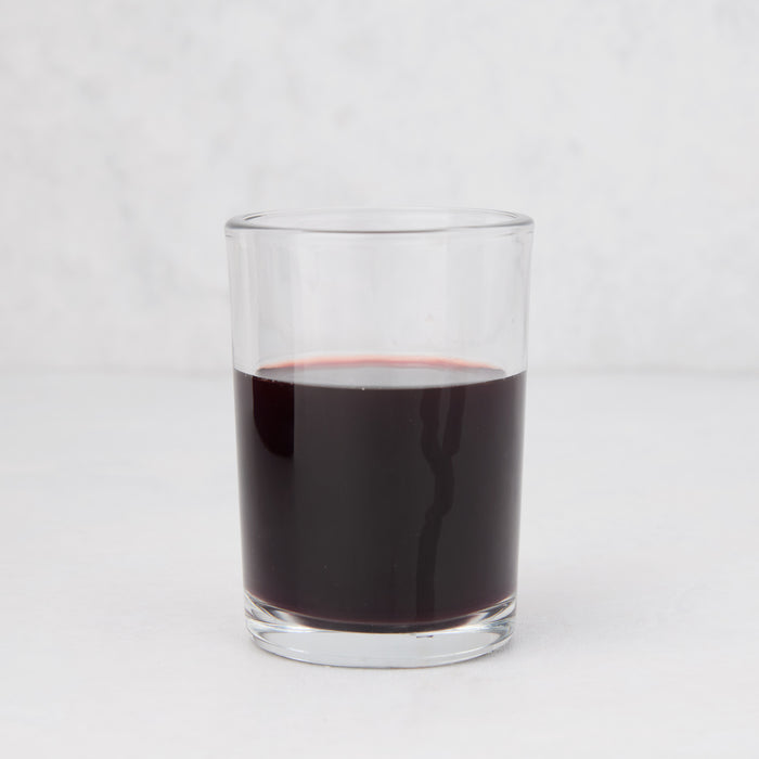 Clear, simple Hudson Grace Everyday Wine Glass filled with red liquid on a white background.