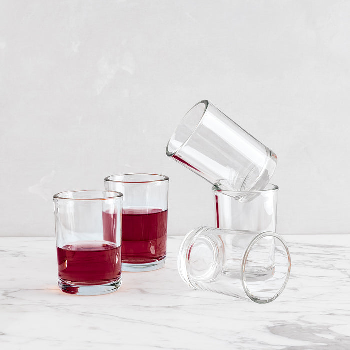 Clear, simple Hudson Grace Everyday Wine Glasses, two filled with red liquid, three empty and stacked.
