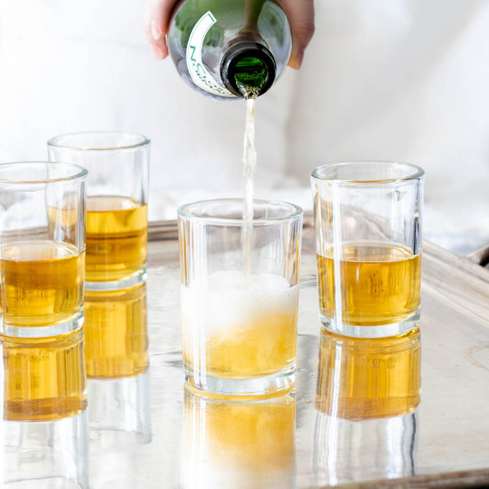 Clear, simple Everyday Wine Glass being filled with a golden beverage from a green bottle.