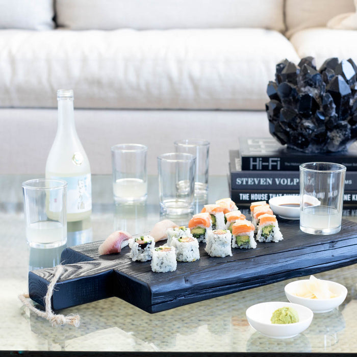 Clear, simple Everyday Wine Glasses on a glass table with sushi, sake, and a dark serving board.