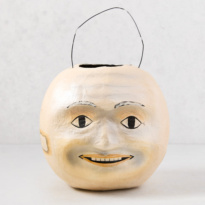 Vintage-style papier-mâché Halloween candy bucket, 10"H, with a distressed cream moon face and black wire handle.