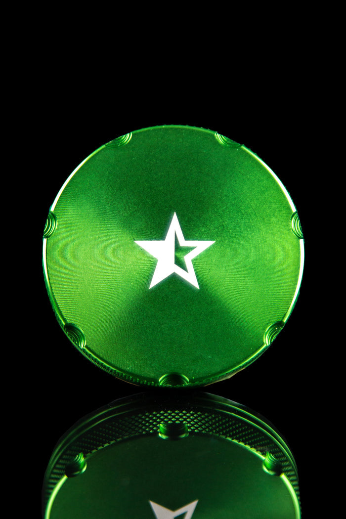 Close-up, top-down view of the Famous X 4-Piece Grinder, showcasing its metallic finish and circular design on a dark background.
