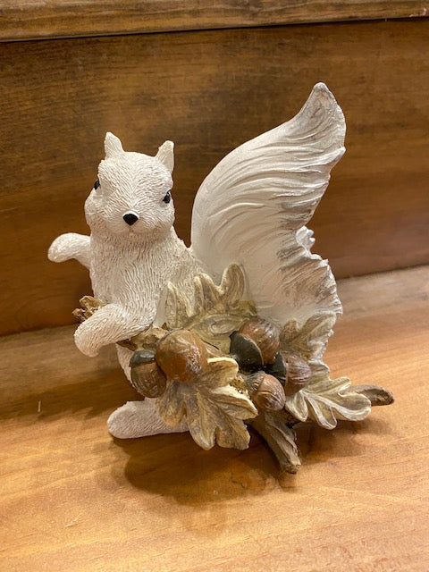 A hand-painted white squirrel resin figurine holding a branch full of acorns.