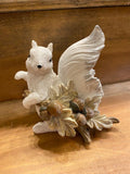 A hand-painted white squirrel resin figurine holding a branch full of acorns.
