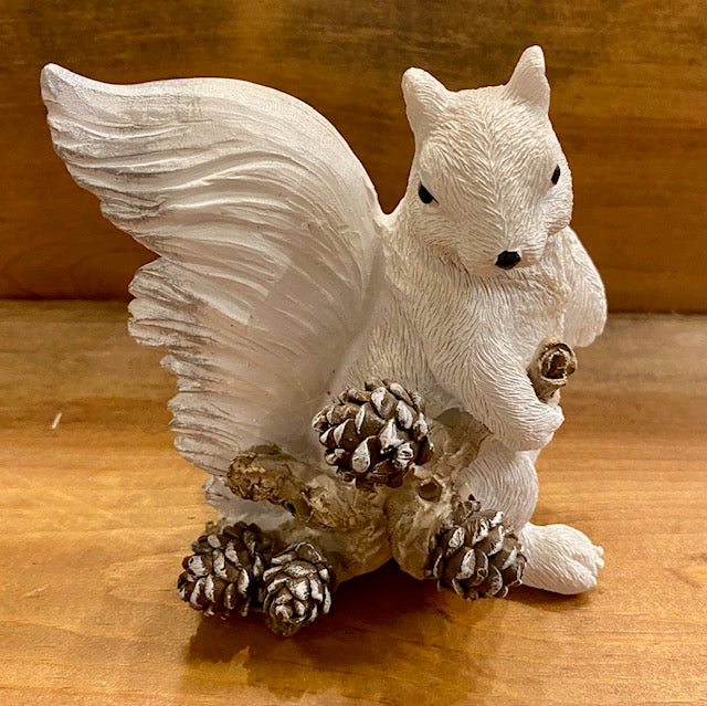 A white squirrel resin figurine holding a branch with pine cones. Side view.