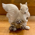 A white squirrel resin figurine holding a branch with pine cones. Side view.