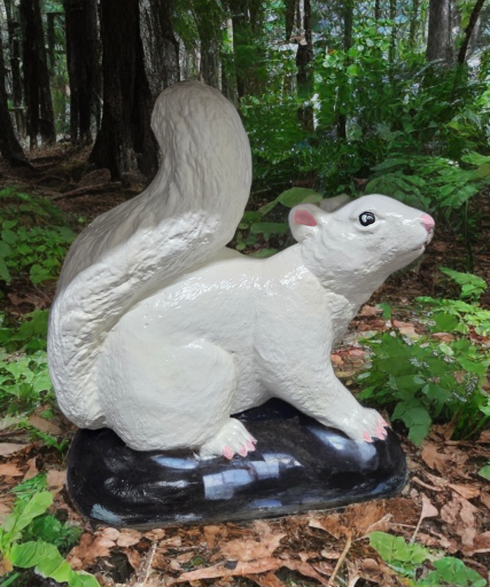 White ceramic chinchilla figurine on a black base in a natural setting with greenery and trees.