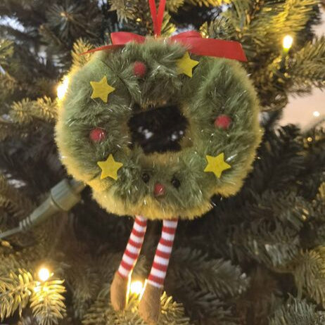 Decorative ornament shaped like a wreath with a face, hanging on a Christmas tree.